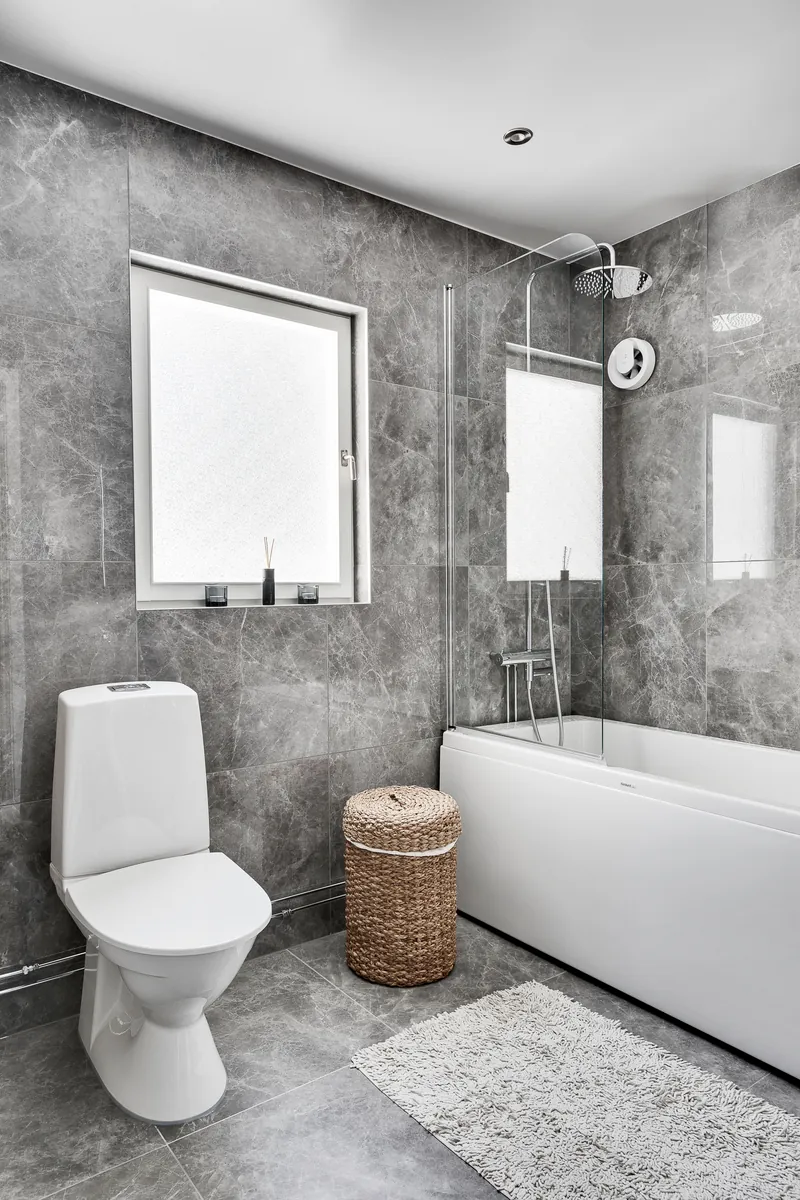 Modernes Bad mit graugeäderten Marmorfliesen, Badewanne mit Glasabtrennung und Duschkopf