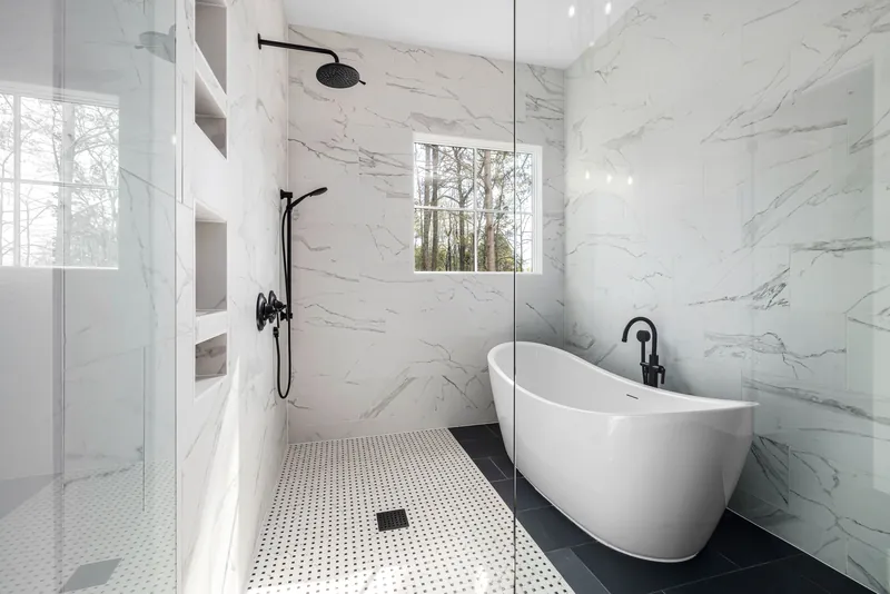 Begehbare Dusche mit weißen Marmorfliesen, schwarzer Armatur und freistehender Badewanne