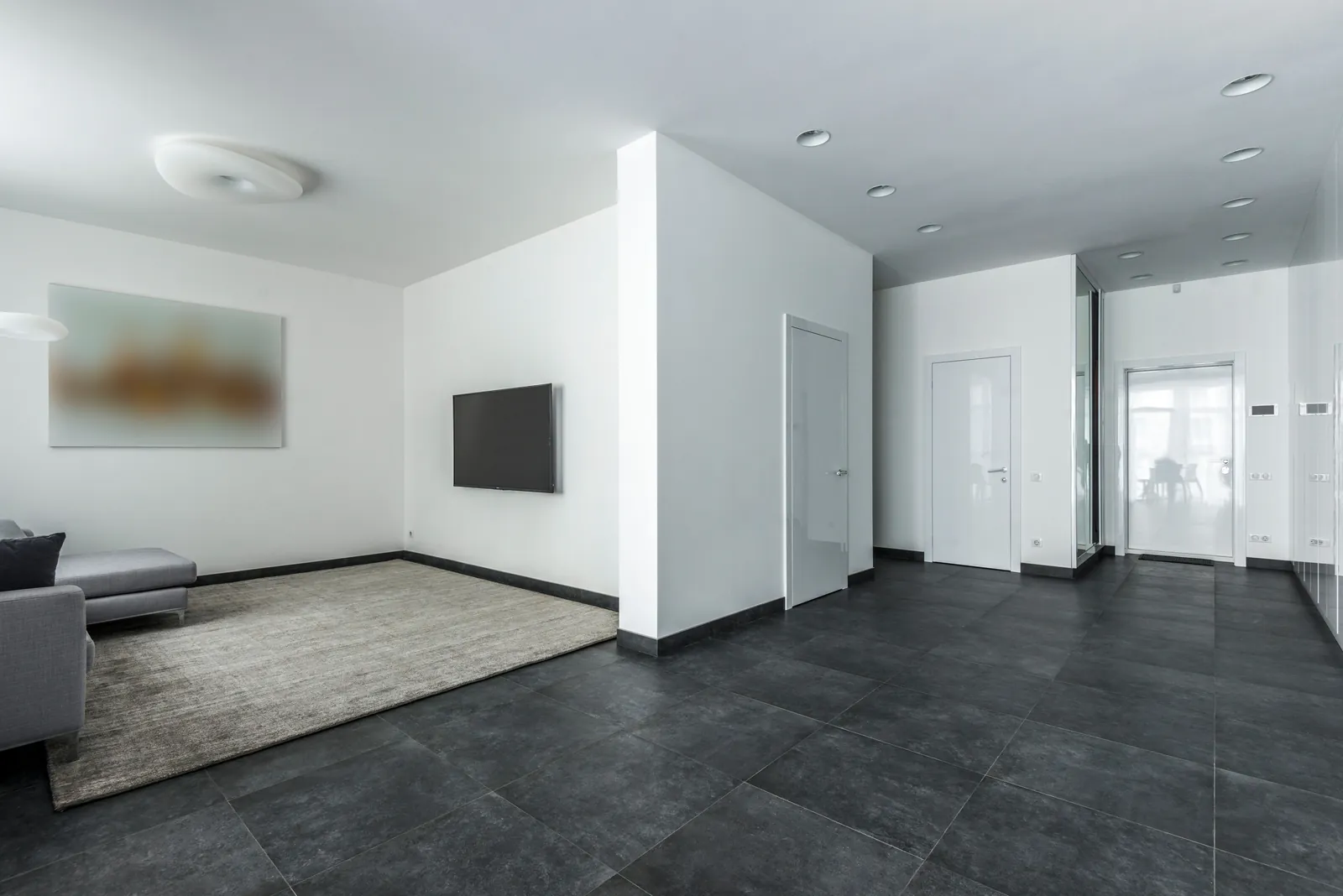 Modernes Wohnzimmer mit großformatigen, dunkelgrauen Fliesen, weißen Wänden und cleanen Türen